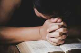 Pessoa orando com mãos cruzadas sobre a bíblia