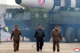 Kim Jong Un e outros dois militares a frente de um veículo militar que carrega um míssil